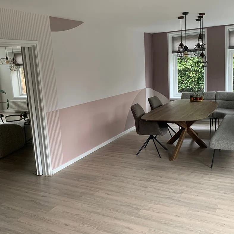 Eetkamer met een oudroze lambrisering, houten eettafel en zwarte hanglampen