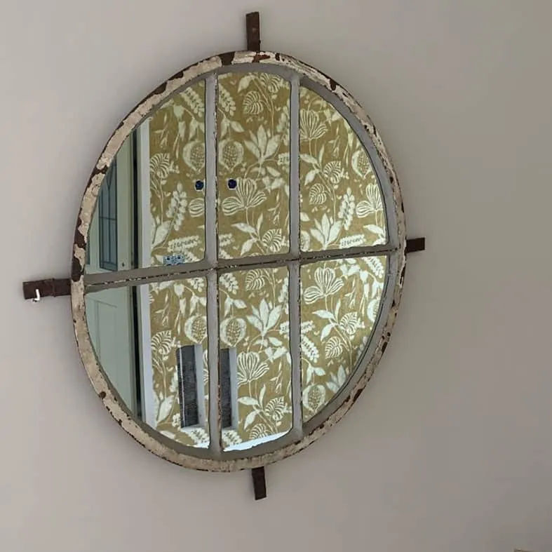 Ronde spiegel met een verweerde lijst voor een wand met olijfgroen bloemenbehang