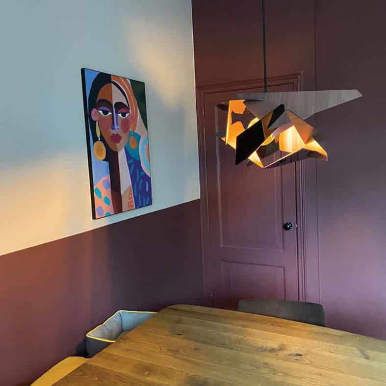 Eetkamer met een bordeauxrode wand, een kleurrijk portret en een geometrische hanglamp
